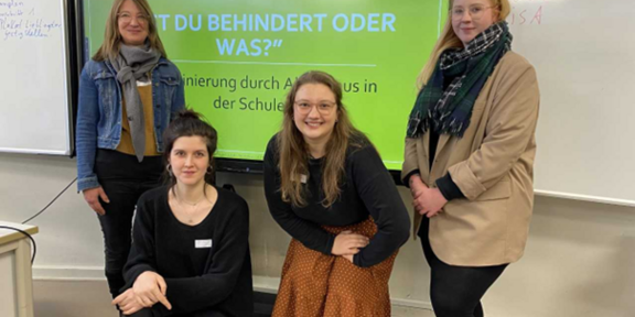 Four women in front of a whiteboard with Power Point turned on. You can see parts of the title "Are you disabled or what?" Discrimination through ableism at school